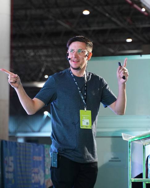 Léo Andrade palestrando no palco, de headset, apontando para os dois lados