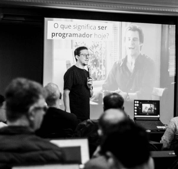 Léo Andrade palestrando para uma sala cheia, com o slide “O que significa ser programador hoje?” projetado atrás