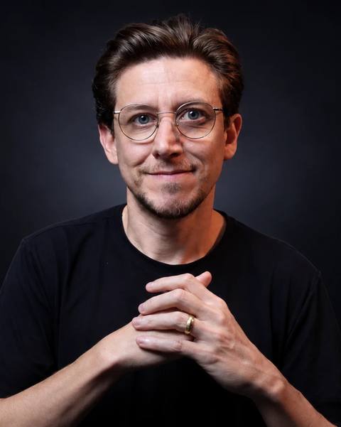 Retrato do Léo Andrade, de camiseta preta e óculos, em fundo preto
