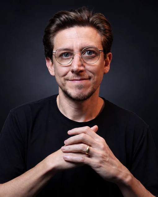 Retrato do Léo Andrade, de camiseta preta e óculos, em fundo preto